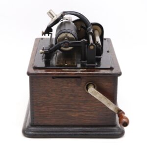 An antique phonograph with a dark wood base, cast iron mechanism, and hand crank is shown from the front, with the cylinder carriage and turntable assembly visible on top.