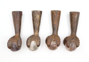 Set of four antique furniture feet with cast iron claw details and glass ball bottoms, shown in a row from different angles.
