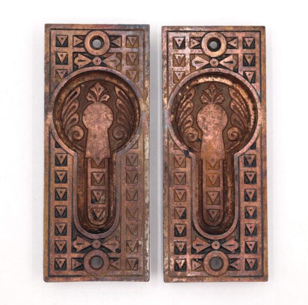 Pair of antique Eastlake cast iron pocket door pulls with a copper finish, shown as a matching pair with recessed oval centers and geometric border details.