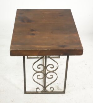 Side table with a dark wood tone pine top and a wrought iron base featuring heart and scroll motifs, shown with visible wear on one front corner.