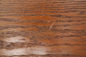 Close-up of a dark wood tone oak bench surface with visible grain, scratches, and worn finish.