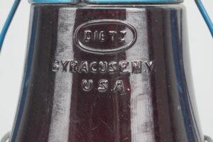 Close-up of a Dietz lantern with a ruby red glass globe and blue metal frame, showing the embossed Dietz Syracuse USA marking.