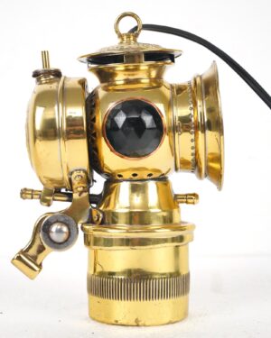 Antique converted bicycle lamp with a polished brass body, a central clear lens, side lens housings, and a black power cord attached.