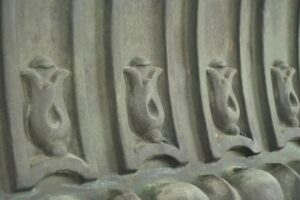 Close-up of a verdigris copper wall art panel with repeating molded decorative details and a weathered surface.