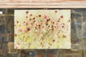 Wall mirror with reclaimed wood molding, silvered glass, and a floral photograph inset at the top.