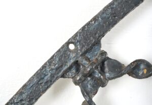 Close-up of an antique Gothic wrought iron window grille with a pointed arch shape, surface rust, and a missing section of the frame.