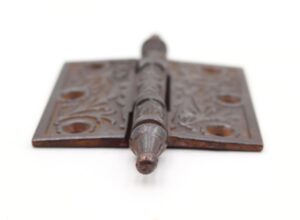 Close-up of a Victorian cast iron butt door hinge with steeple tip, three knuckles, and decorative cutout pattern.