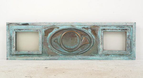 Rectangular window panel with two clear side panes and a raised post horn medallion in the center, showing a heavily worn verdigris finish.