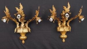 Pair of Rococo Revival wall sconces in gilt brass, shown as a matching pair with ornate foliate arms and three bulb sockets each.