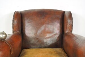 Close-up of a brown leather club chair with nailhead trim and a visible ashtray strap on the arm.