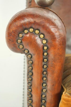 Close-up of the leather chair arm with brass nailhead trim and worn surface detail.