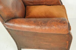 Close-up of a brown leather club chair with a studded armrest and cushioned seat edge.