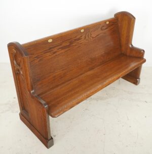 Dark oak church pew bench with a slanted seat, Gothic side carvings, and brass seat-number plaques visible along the back.