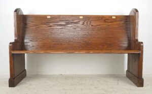 Front view of a Gothic oak church pew bench with a slanted seat, dark wood tone, Gothic side carvings, and oval brass plaques marked 17, 18, and 19 on the backrest.