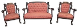 Victorian three-piece seating set with a settee and two armchairs, showing dark wood frames, red tufted upholstery, and ornate carved arms and backs.