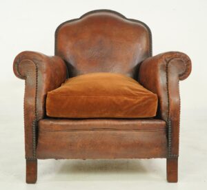 Art Deco brown leather club chair with a mustache-shaped back, round armrests, a velvet seat cushion, and studded trim.