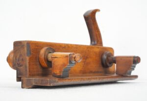 Antique wooden plow molding plane shown in a close-up side view with a medium wood tone body, steel hardware, and visible wear from use.