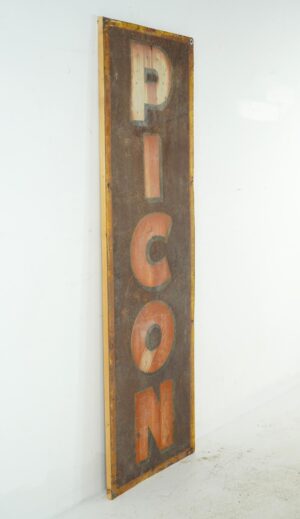 Vintage French Picon advertising sign in a tall vertical format, showing worn multicolor lettering on a brown enamel steel panel with rusted edges and wood backing.