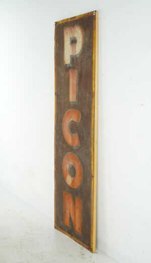 Vintage French Picon advertising sign made of enameled steel, shown in a tall narrow view with large vertical letters, surface wear, rust, and wood backing visible at the edge.