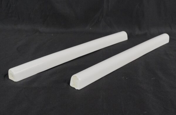 Pair of white glazed ceramic pencil wall tiles shown as two rounded strips, one slightly closer to the camera than the other.