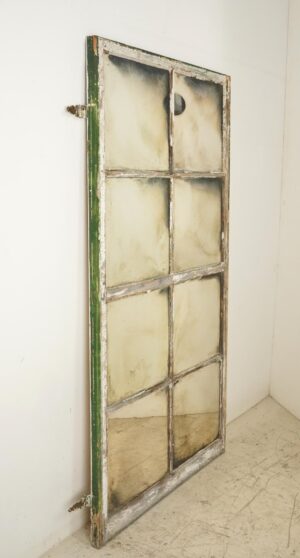 Tall handcrafted wall mirror made from a reclaimed window frame, with eight pane divisions, a green and white worn wood border, and original hinges attached on the left side.