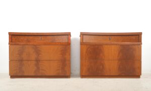 Pair of vintage bedside cabinets shown side by side, each with three drawers, gently curved tops, dark wood tone veneer, and brass key-shaped pulls.