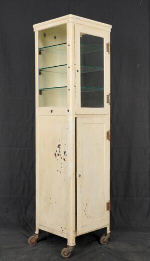 Tall narrow medicine cabinet with a glass upper door, three interior glass shelves, and a solid lower door on caster wheels.