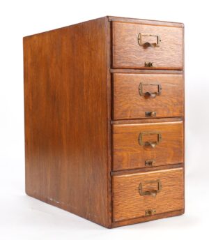 Four-drawer oak desktop file cabinet with brass hardware, shown at a three-quarter angle with built-in card filing handles on each drawer.