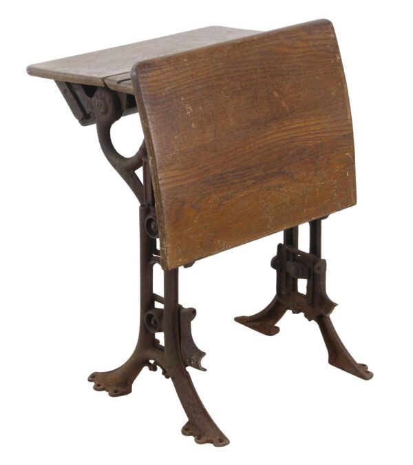 Antique folding school row desk with a dark wood top and seat on cast iron legs, shown in a folded side view.