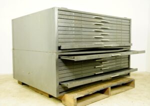 Gray steel flat filing cabinet with multiple shallow drawers, several drawers partly open and one fold-out shelf extended on the front.
