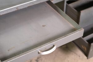 Open gray steel desk tray with a curved pull handle and visible wear.