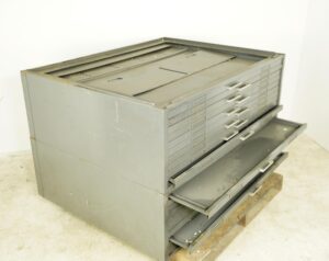 Gray flat filing cabinet with multiple shallow drawers, several drawers pulled open, shown at an angle.