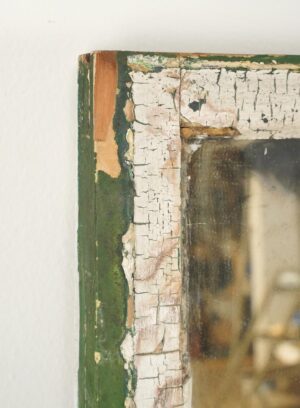 Close-up of a handcrafted window mirror with a distressed green and white wood frame and a silvered pane.