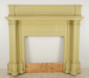 Colonial Revival wood mantel with fluted pilasters and a large opening, painted in muted yellow-green.