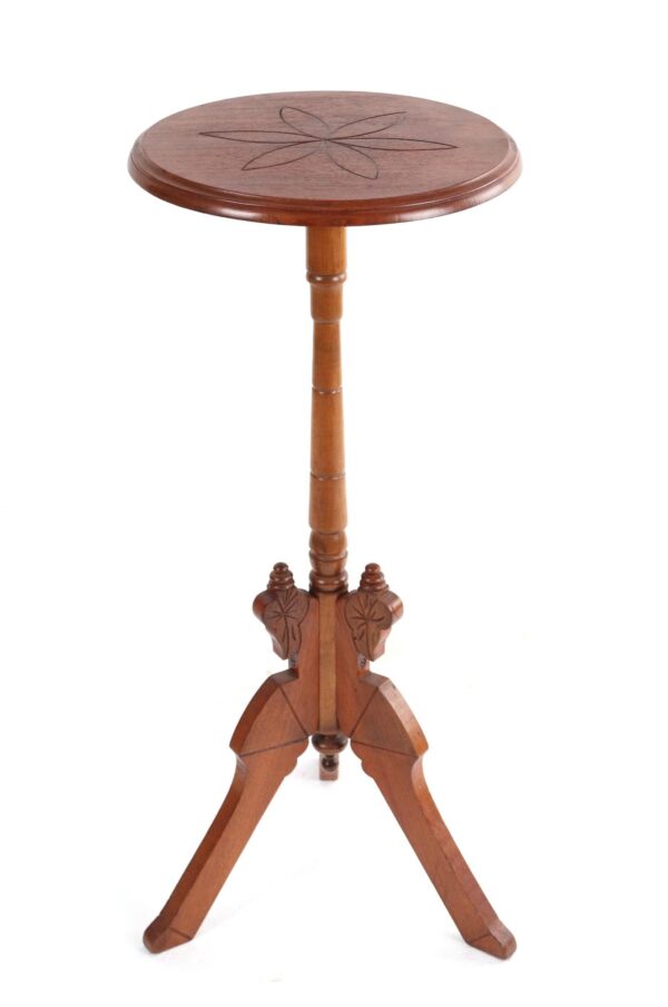 Wooden plant stand with a round top, turned central post, and three carved legs, shown from the front with a six-petal flower motif on the tabletop.