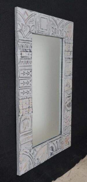 Handcrafted wall mirror with a patchwork tin ceiling tile frame in gray and white, shown at a slight angle with the reflective center visible.