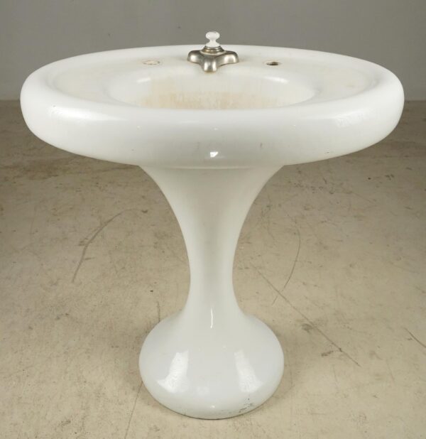 White pedestal sink with a curved base, a single center faucet, and visible bowl staining.