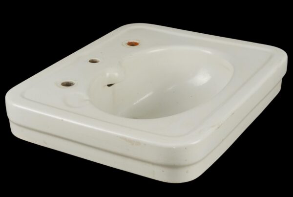 Vintage white ceramic wall sink with an oval basin, three faucet holes, and visible staining and surface wear around the openings and bowl.