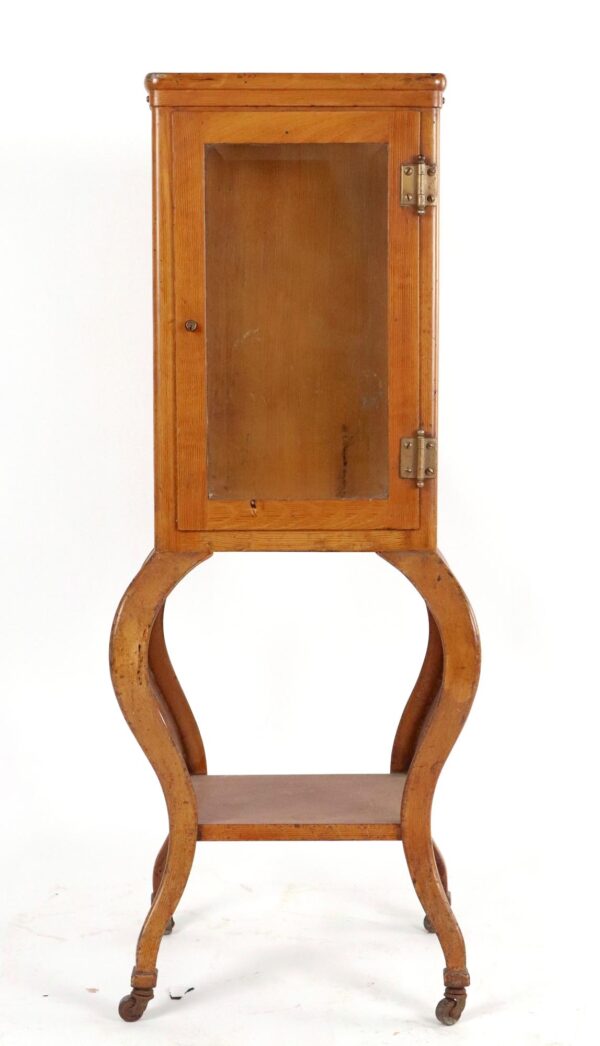 Tall narrow medical display cabinet with a front glass door, curved side supports, and casters, shown in a straight-on view.