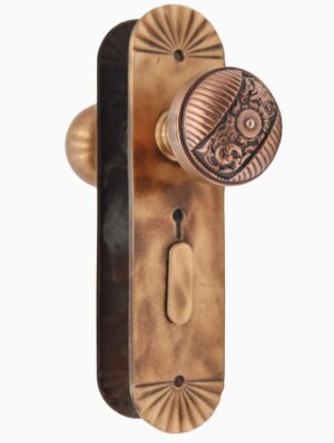 Antique brass entry door knob set with a decorative round knob, keyhole opening, and elongated backplate shown in close-up.