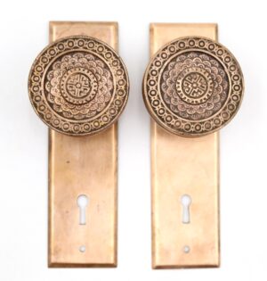 Pair of antique brass dummy door knobs on rectangular back plates, each with an ornate circular rosette and keyhole cutout.