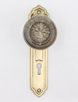 Vintage Art Deco dummy door knob set with a clear glass knob and polished brass back plate, shown front on with keyhole cutout and mounting holes visible.