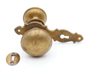 Vintage brass passage door knob set with two round knobs, one decorative back plate, a rosette, and a keyhole cover.