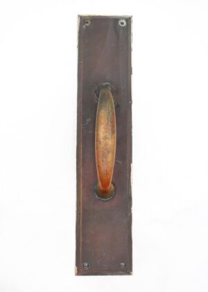 Vintage commercial bronze door pull with an antique finish and visible mounting screws, shown vertically on a rectangular backplate with surface wear from prior use.