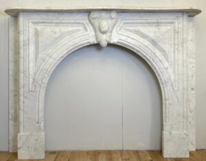 Neoclassical white marble fireplace mantel with gray veining, featuring a large arched opening and symmetrical carved details.
