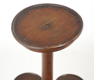 Close-up of a Victorian freestanding plant stand with a round dark wood top and visible wear along the rim.