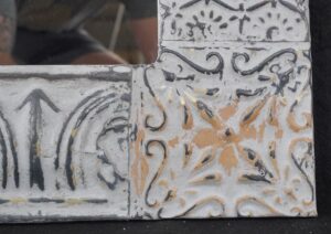 Patchwork tin wall mirror with embossed decorative panels in gray and white, shown in close-up.