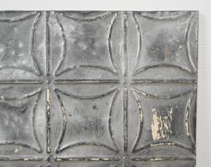 Handcrafted gray tin wall panel with a raised geometric grid and worn antique surface showing patches of exposed wear.