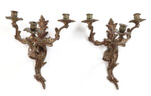Pair of Louis XV style bronze wall sconces with foliate scrollwork and three candle cups on each piece, shown as a matching pair.