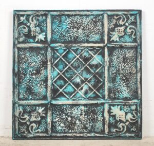 Handcrafted tin wall panel with a grid of textured sections and ornate corner details in black, blue, and white.